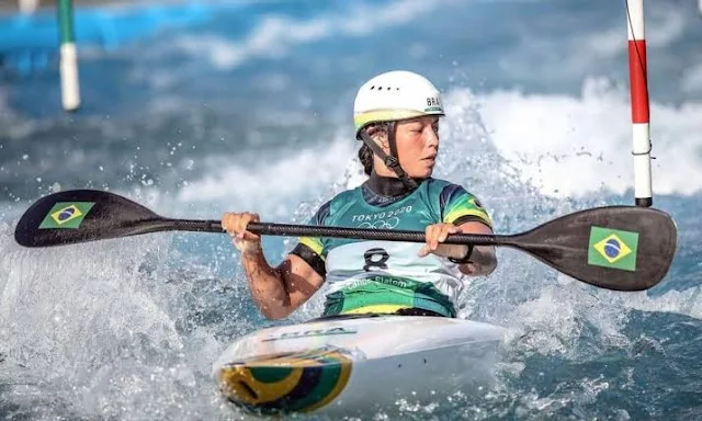 Morena e de capacete branco, Ana está com a pá na sua mão, olhando para o lado e controlando o barco na correnteza