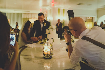 Novios cortando la tarta mientras el fotógrafo y una invitada con móvil les hacen una foto