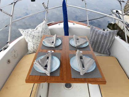 The cockpit of a boat with the tiller folded back out of the way and a nicely set table laid out.