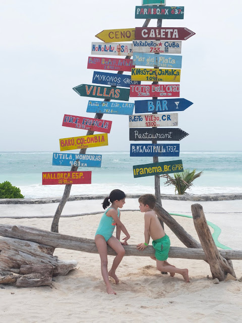 Dos niños en la playa frente a unos carteles de colores con distancias a ciudades del mundo