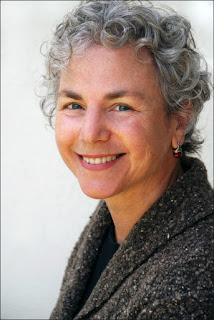 Image of Ellen Bass wearing a brown, gray, and white boucle wool sweater. She smiles at the camera. She has short, gray, curly hair, and blue eyes.