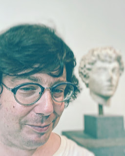 Greig poses in front of a bust of a youthful Marcus Aurelius.