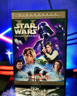 The DVD of Star Wars episode five the Empire strikes back sits in front of a television screen, displaying the light saber duel between Darth Vader and Luke Skywalker.