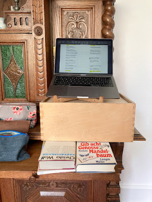 Bücher und Holzkiste seitlich auf einem alten Buffet bieten einen erhöhten Arbeitsplatz