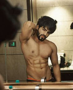 A bodybuilder taking off his shirt and looking at himself in the mirror