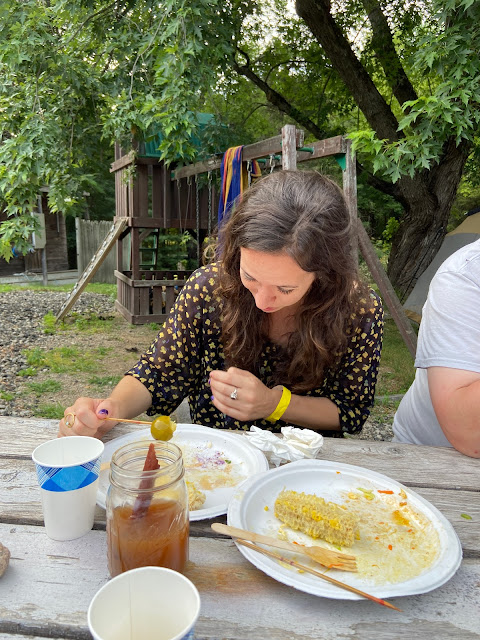 a woman sitting at a picnic table holds a pickled lime on a skewer over a paper plate