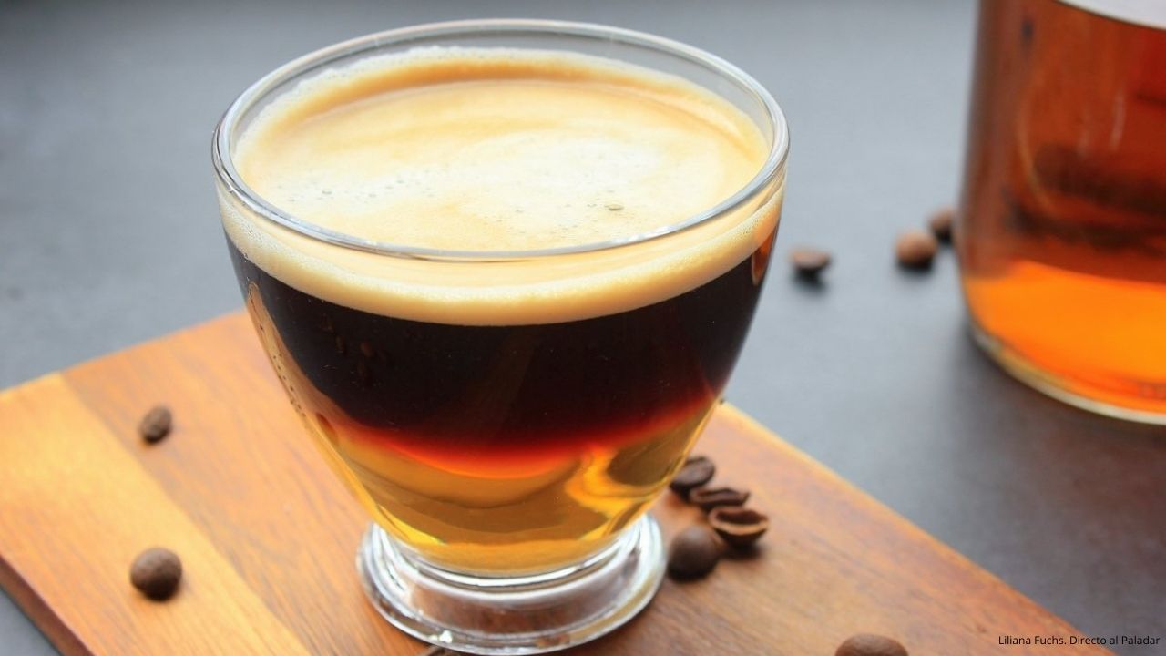 Vasos de carajillo servidos sobre platos blancos, con una capa de café oscuro y licor dorado, acompañados de cucharillas.