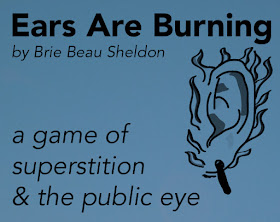 a dark blue box with the text "Ears Are Burning by Brie Beau Sheldon, a game of superstition & the public eye"