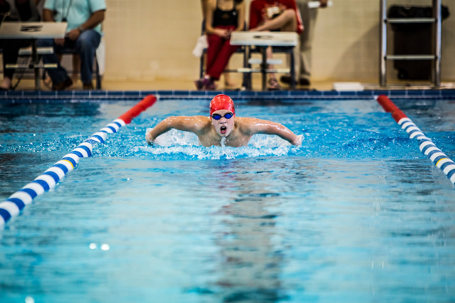 A photo of a person in a large swimming pool swimming intensely towards the camera.