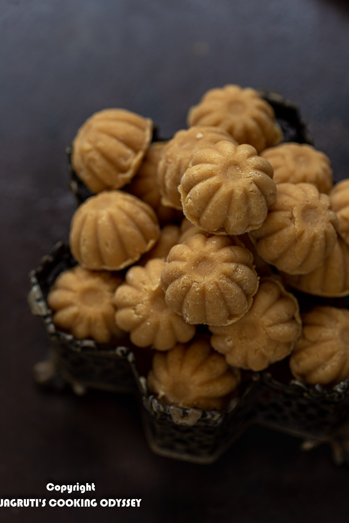 A close up image of no added sugar slow roasted mawa peda arranged in a vintage metal box on very dark brown backdrop