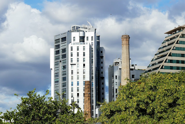 Edificios altos y modernos junto a chimeneas de antiguas fábricas y árboles