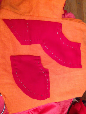 Two pieces of screaming red fabric with pinned keyhole collar designs on them, laid out on bright-orange fabric.