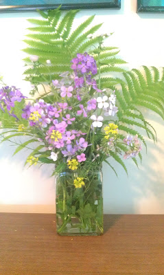 White, purple, and yellow flowers in a vase with ferns.