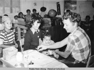 A nurse preparing a vaccine for a baby sitting on a woman's lap. A young boy stands behind the woman's chair.