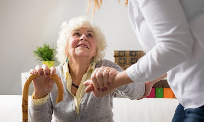 home care aide helps a senior woman get up