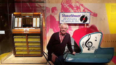 Mit einer Musikbox von 1957 und einer Chaise aus einer Kirmes-Raupen-Bahn von 1948 begann der Rundgang in der Essener Ausstellung auf Zollverein. Zur Erinnerung ließ sich Michael Winkler davor ablichten. (Foto: Werner Homann)