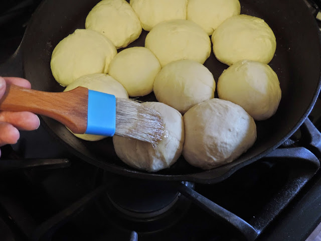 The raised dinner roll dough being brushed with egg whites.