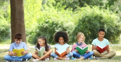 Four children, two girls and two boys, are sitting in a line on the grass and reading their books.