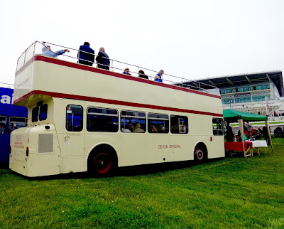 A cream and red, double decker bus parked near the race course in Epsom