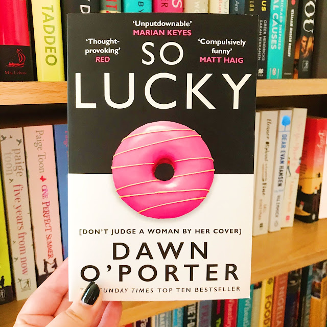 So Lucky by Dawn O'Porter held up in front of bookshelf