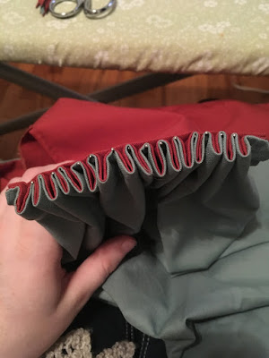 An end-on photo of small pleats pinned in the valleys to another, flat, piece of fabric. The pleated fabric is red lined with grey-blue, which makes them pretty thick.