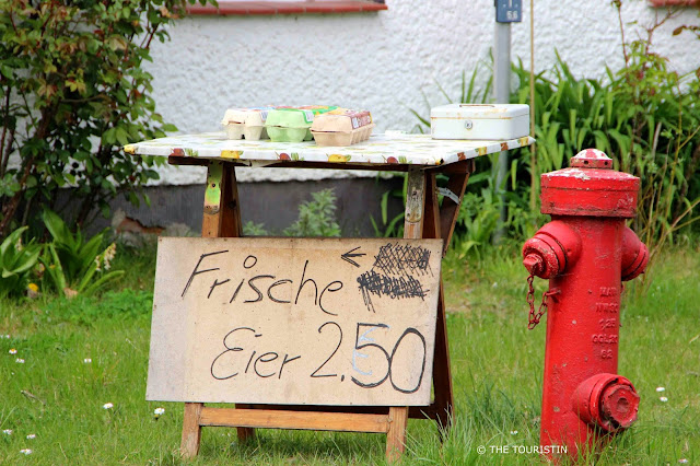  A red water hydrant next to a table selling 10 eggs for EUR 2.50 which has to be paid cash into a money box sitting on the table also..