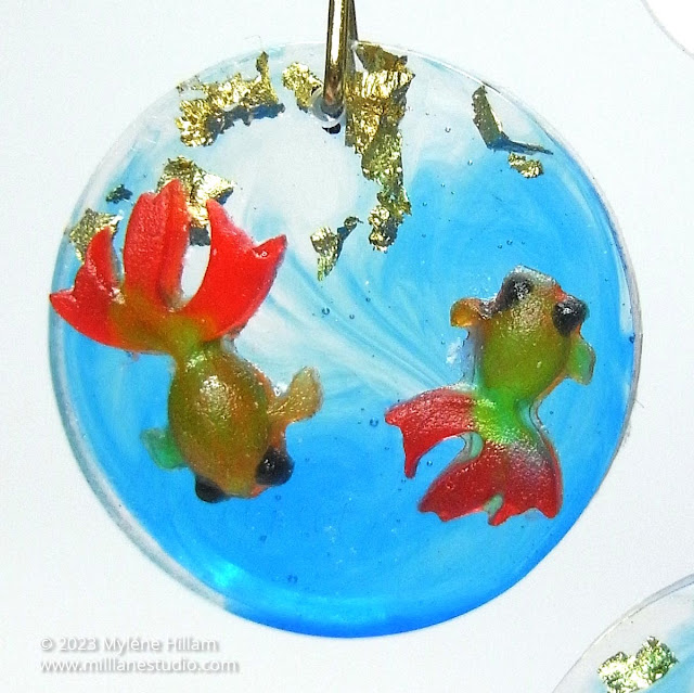Two miniature goldfish on a blue and clear resin circle with goldleaf flakes