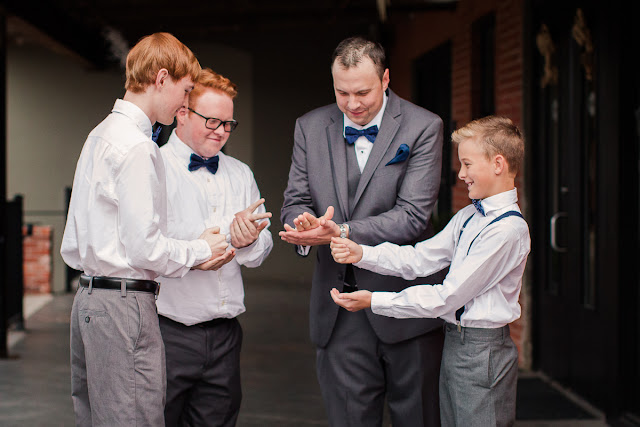 Andy playing Paper Rock Scissors with his younger generation of male family members.  Together they are all sporting white shirts and blue bowties.  Set at the Hall at the Railhouse located in Norman, OK during the fall of 2016.