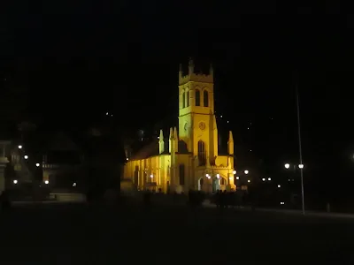 Christ Church in Shimla beautifully illuminated at night, with its Gothic-style architecture glowing under soft yellow lighting.
