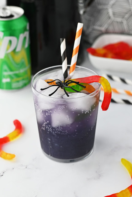 drink in a glass with straws, gummy worms and a plastic spider.
