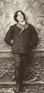 A young Oscar Wilde wearing a Smoking Jacket and leaning against an exuberantly decorated backdrop during a photography session.