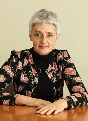 Ana María del Río (Foto en color; la autora de frente a la cámara sentada ante una mesa).