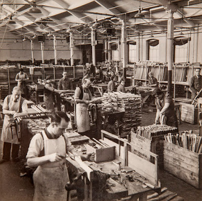 A sepia photograph of a dozen workers, male and female, making rifle furniture