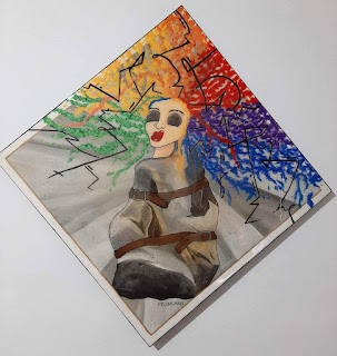 A mixed media painting by Melanie Cable. It's a self portrait, of a woman in a straight jacket, with buttons for eyes and wild rainbow hair sticking out in all directions.