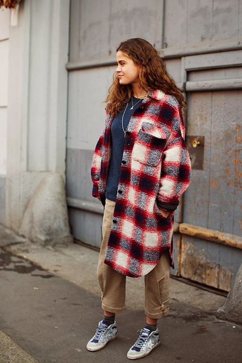 young woman wearing stylish grunge outfit with oversized flannel shirt is posing on a street