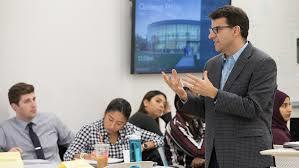 A man in a grey suit and tie explaining about MBA, online, business,prerequisites, business schools, courses and online MBA.