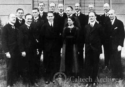 foto de um grupo de cerca de quinze físicos mais famosos da época reunidos em uma conferência com todos em pé e apenas Lise Meitner de mulher presente no centro da foto ao lado de Niels Bohr