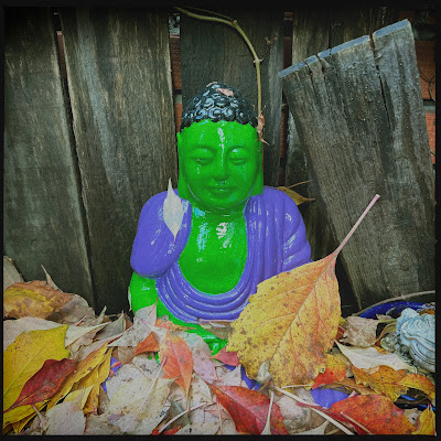 In hulk-kleuren beschilderde boeddah omgeven door herfstbladeren