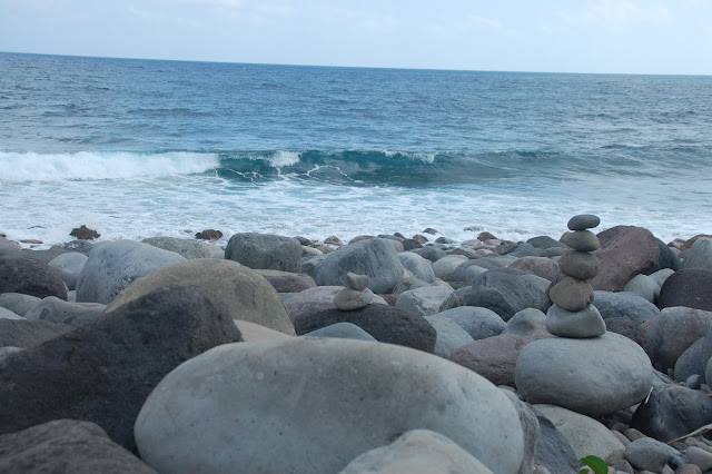 A stack of pebbles amidst rounded boulders while strong waves slam towards the beach at the Valugan Boulder Beach in Batanes