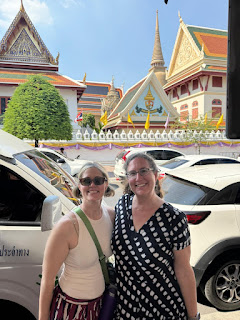 Two women posing on a street in Thailand in front of ornate temples