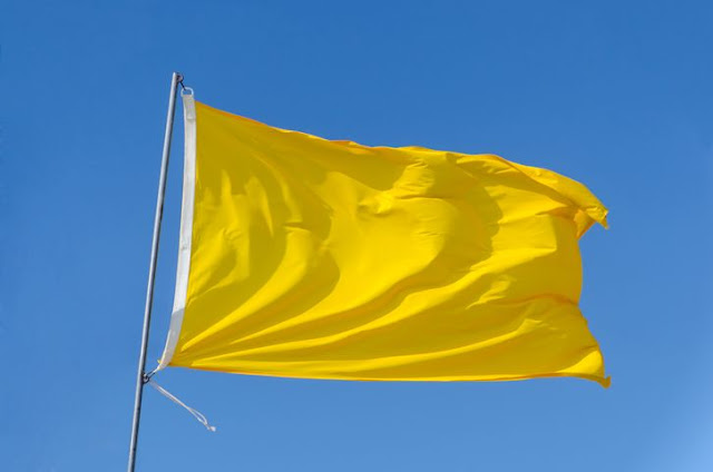 Bendera Kuning Sebagai Simbol Kematian, Bagaimana Sejarahnya? National Geographic Indonesia - Rabu, 24 April 2019 | 17:59 WIB     Ilustrasi bendera kuning.Photitos2016/Getty Images/iStockphoto Ilustrasi bendera kuning.  Nationalgeographic.co.id - Warna hitam sering dikaitkan dengan suasana duka atau kematian. Di beberapa negara, pakaian hitam biasa dikenakan saat menghadiri pemakaman. Warna gelap tersebut seolah-olah menggambarkan kesedihan dan kemuraman setelah ditinggal orang terkasih.   Namun, selain hitam, di beberapa wilayah Indonesia, kuning juga menjadi warna kematian. Disimbolkan melalui bendera-bendera yang dipasang di sekitar rumah duka. Bagaimana awal mulanya?  Baca Juga : Kesaksian Semesta Karena Ulah Gelegar Tambora  Dilansir dari intisari.grid.id, pemilihan kuning sebagai warna kematian ini ternyata bermula dari zaman kolonialisme Belanda. Awalnya, dikenal bendera persegi panjang polos berwarna kuning dengan simbol huruf Q.  Bendera kuning ini merupakan penanda bagi para penderita sebuah wabah mematikan yang wajib dikarantina. Oleh sebab itu, simbolnya adalah Q, berasal dari kata "quarantine".  Baca Juga : Kesaksian Perwira VOC Ketika Prahara 1740 di Tangerang     Konon, di zaman itu, saking mematikannya, wabah tersebut cepat menular dan memakan banyak korban meninggal. Banyak bendera kuning lalu terlihat di setiap kematian.  Hingga saat ini, kebiasaan itu masih dilakukan, meskipun sudah tidak ada wabah. Dan bendera kuning pada akhirnya identik dengan kematian dan digunakan untuk menandai kematian seseorang.