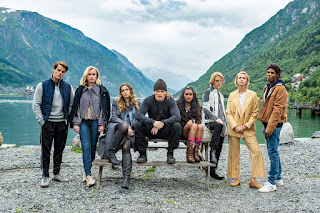 Cast of Ragnarok sitting on a bench beside a lake, mountains in background