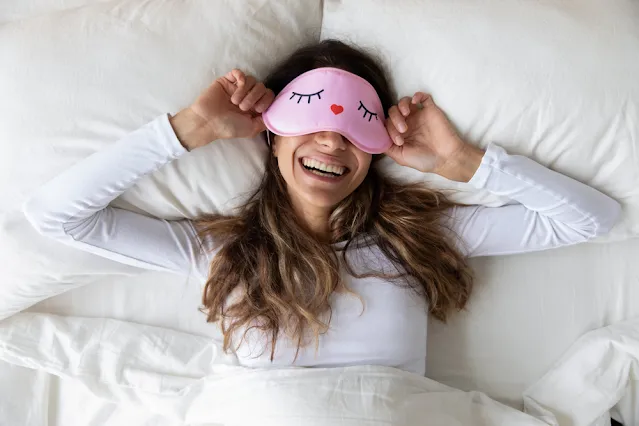 Above top view head shot of happy, mixed race, healthy woman living in bed with sleep mask, waking up from sweet dreams. Smiling relaxed young woman feeling energetic in the morning at home.