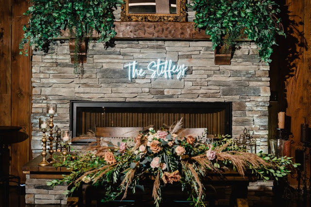 stone mandle behind sweetheart table with greenery and neon wedding sign