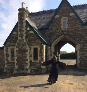 Woman in a black dress twirling in front of a large stone carriage-arch house