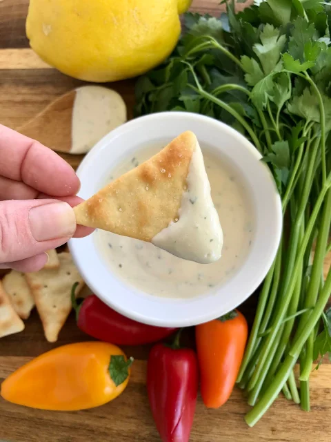 Lemon garlic tahini sauce being scooped onto a pita cracker.