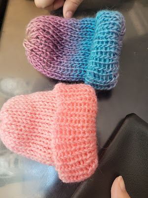 Two knit baby hats are on a transparent table. One is a blush pink and the other is blue with hints of purple.