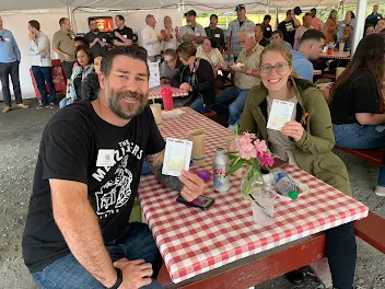 man and woman sitting at picnic table holding up gift card prizes for winning skee ball