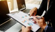 Two professionals analyzing marketing data with charts and graphs on a clipboard, representing digital marketing strategies in Italy