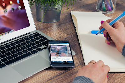 a computer, a phone and a hand with a pen and book